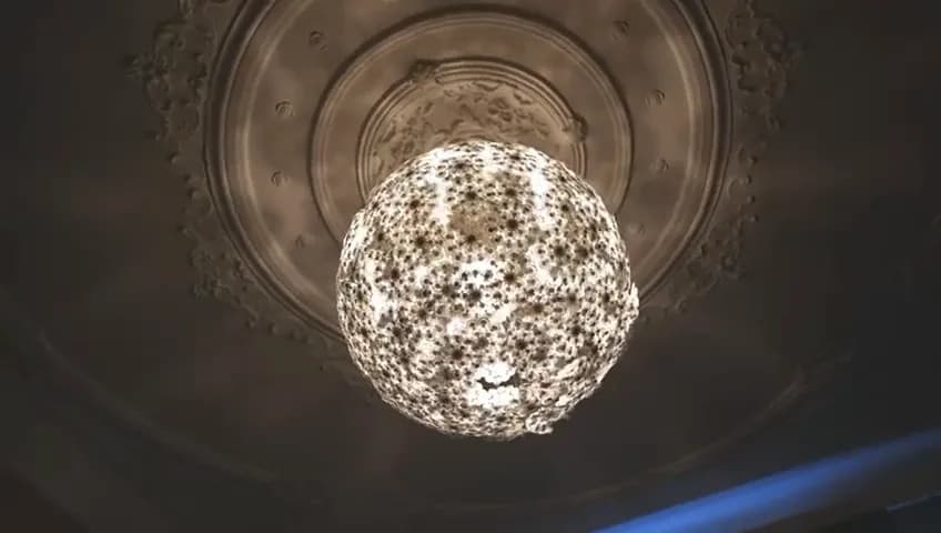 Looking straight up at a glowing, patterned globe lamp hanging from an ornate ceiling rose.