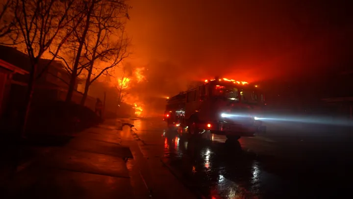A fire engine on a wet road at night, its lights cutting through smoke.