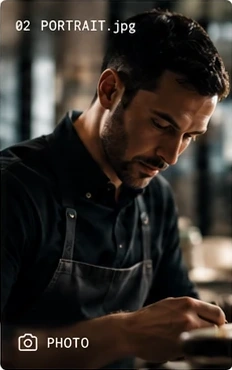 A chef in a dark shirt and apron, head bowed as he plates.