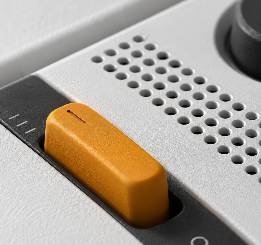 Close up, an orange fader in its dark track beside a perforated grille, the grain of the white casing sharp