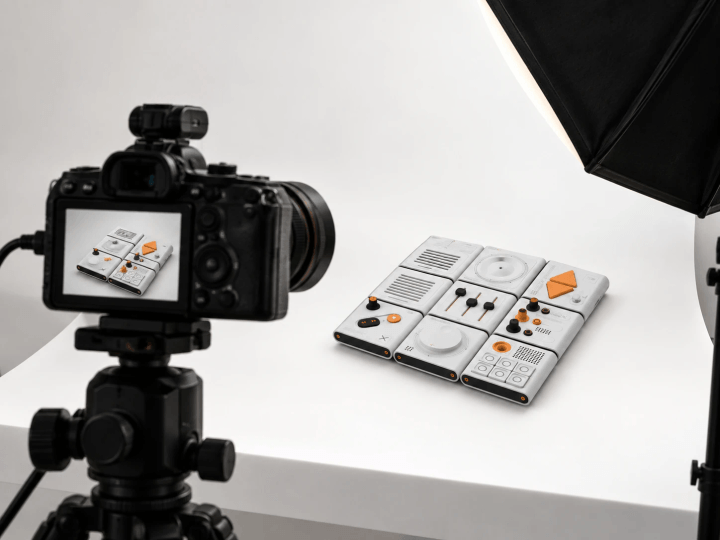 A camera on a tripod in a white studio, framing the modules on the table under a softbox
