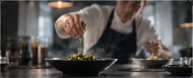 A cook scatters herbs over a bowl on a kitchen counter.